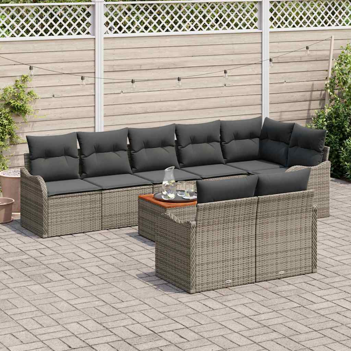 Geflochtenes Outdoor-Ecksofa mit grauen Kissen. Ein Holztisch mit Krug und Gläsern steht in der Mitte. Im Hintergrund befindet sich ein Zaun.