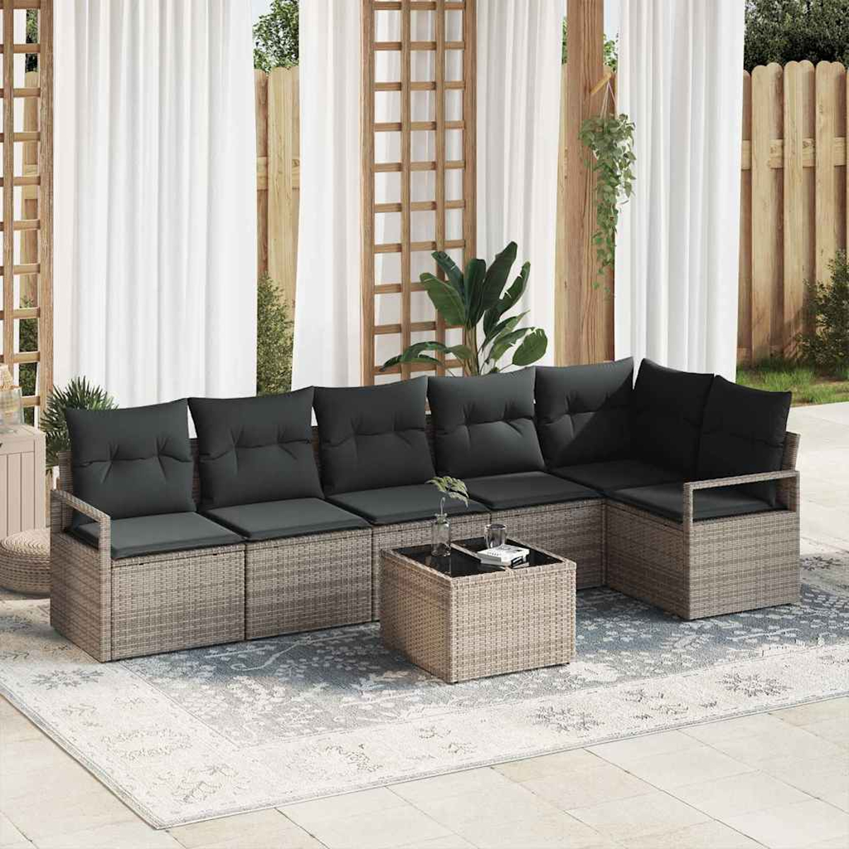 Outdoor-Ecksofa mit grauen Kissen und einem passenden Couchtisch auf einem gemusterten Teppich, vor weißen Vorhängen und Holzbalken.