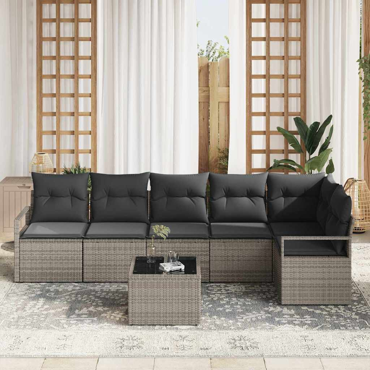 Outdoor-Ecksofa mit grauen Kissen und einem kleinen Tisch auf einem gemusterten Teppich. Weiße Vorhänge und Holzrahmen sind sichtbar.