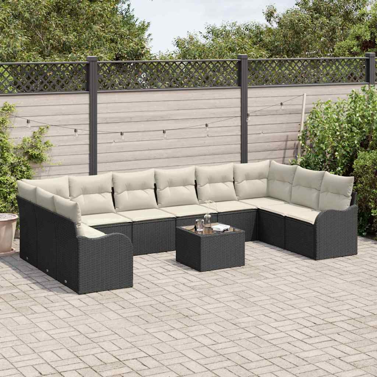 Eine Terrasse mit einem schwarzen Ecksofa aus Korbgeflecht mit beigefarbenen Kissen. Davor steht ein kleiner quadratischer Tisch mit Gläsern.
