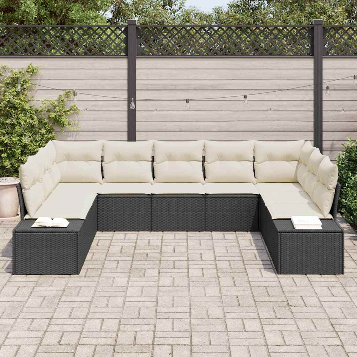 Dunkelgraues Korbmöbel-Ecksofa mit cremefarbenen Kissen auf einer Terrasse. Auf beiden Enden liegt ein Buch. Im Hintergrund ein Holzzaun.