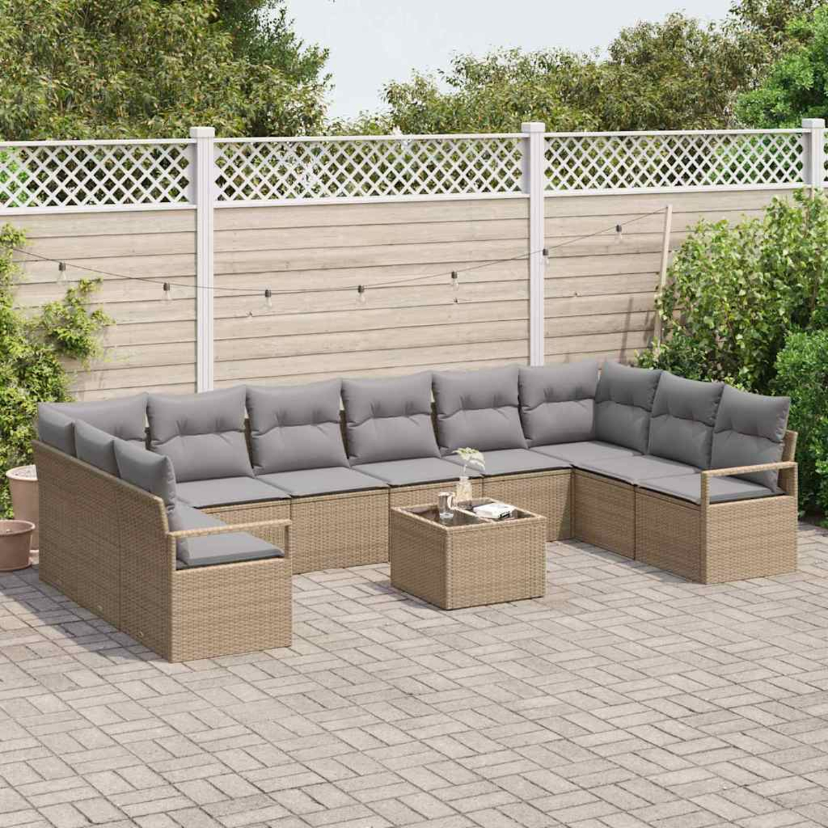 Outdoor-Rattan-Ecksofa mit grauen Kissen, quadratischer Couchtisch, auf gepflasterter Terrasse. Zaun und Bäume im Hintergrund.