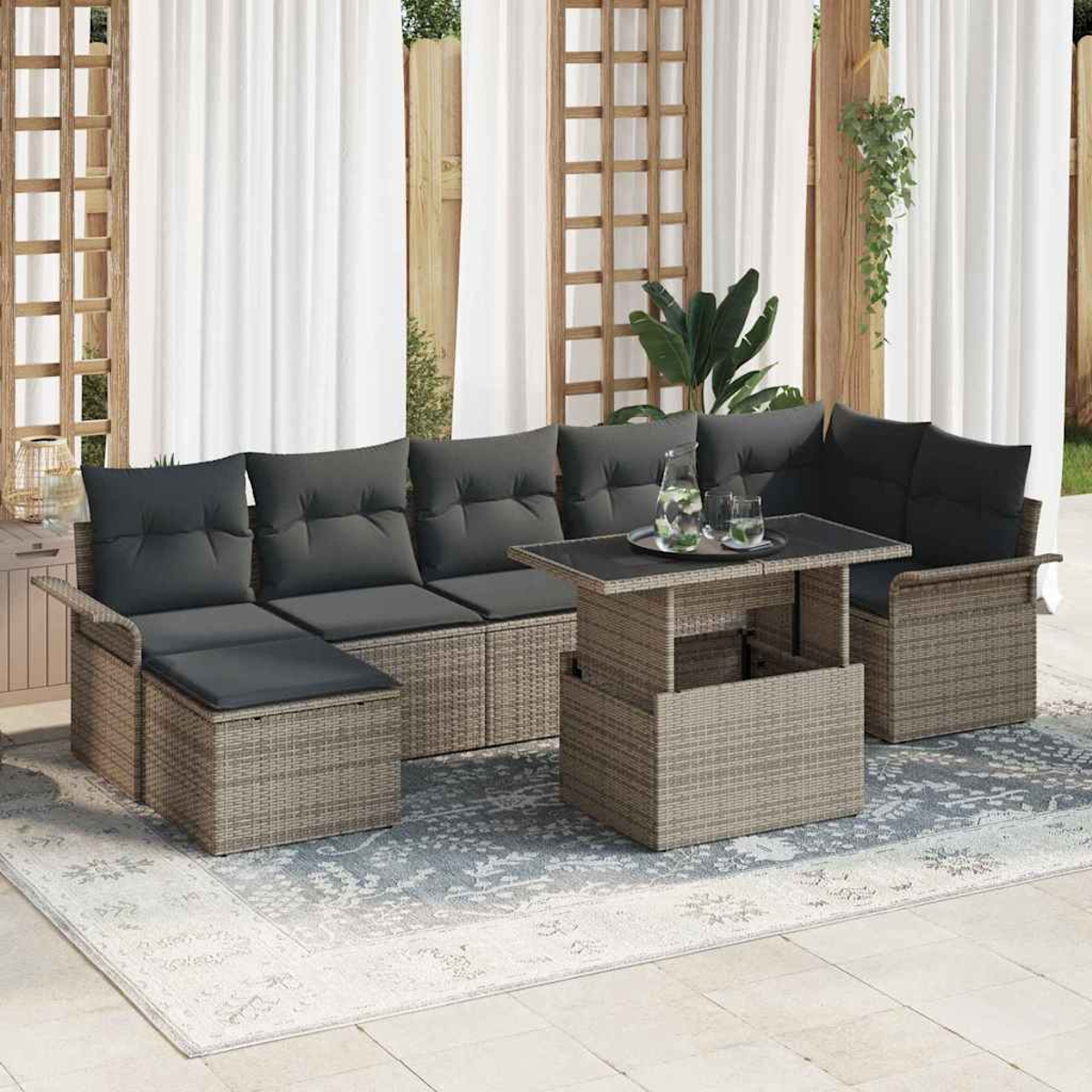 Gartenmöbel-Set aus Korbgeflecht mit dunkelgrauen Kissen. Enthält ein Sofa, zwei Stühle und einen Couchtisch mit Hubfunktion, auf einem gemusterten Teppich.