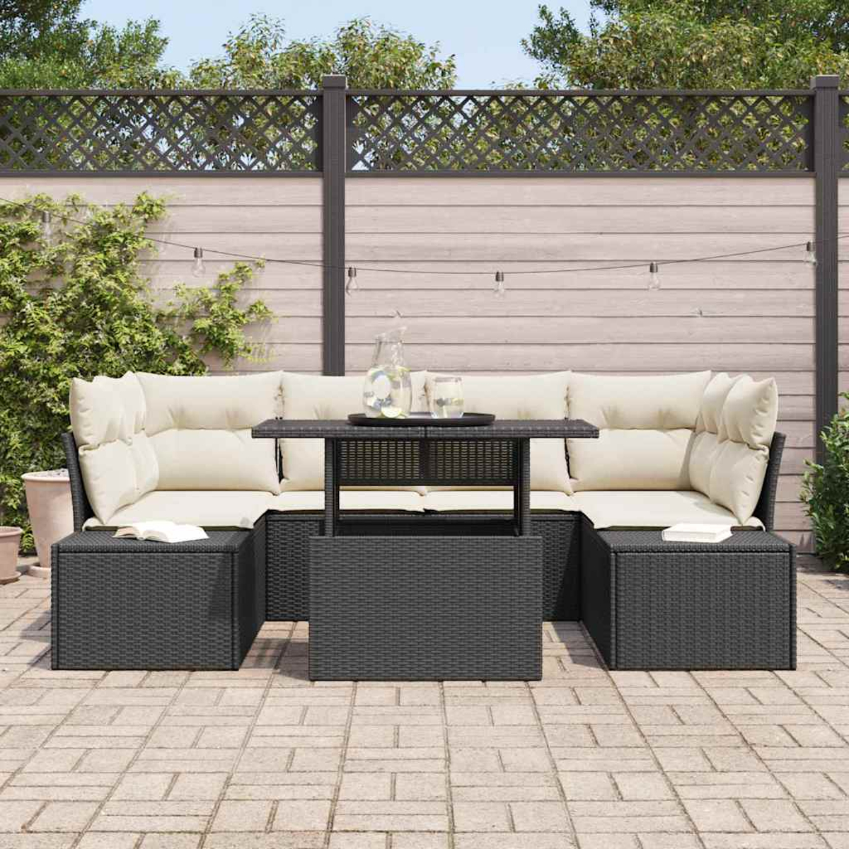 Garten-Sitzgruppe mit beigefarbenen Kissen, einem dunklen Tisch und zwei Ottomanen. Im Hintergrund ein Zaun mit Lichterketten.