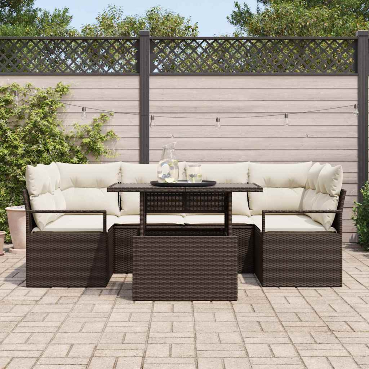 Terrassenset im Freien mit braunen Korbmöbeln, cremefarbenen Kissen und einem kleinen Tisch. Hintergrund mit Holzzaun und grünen Pflanzen.