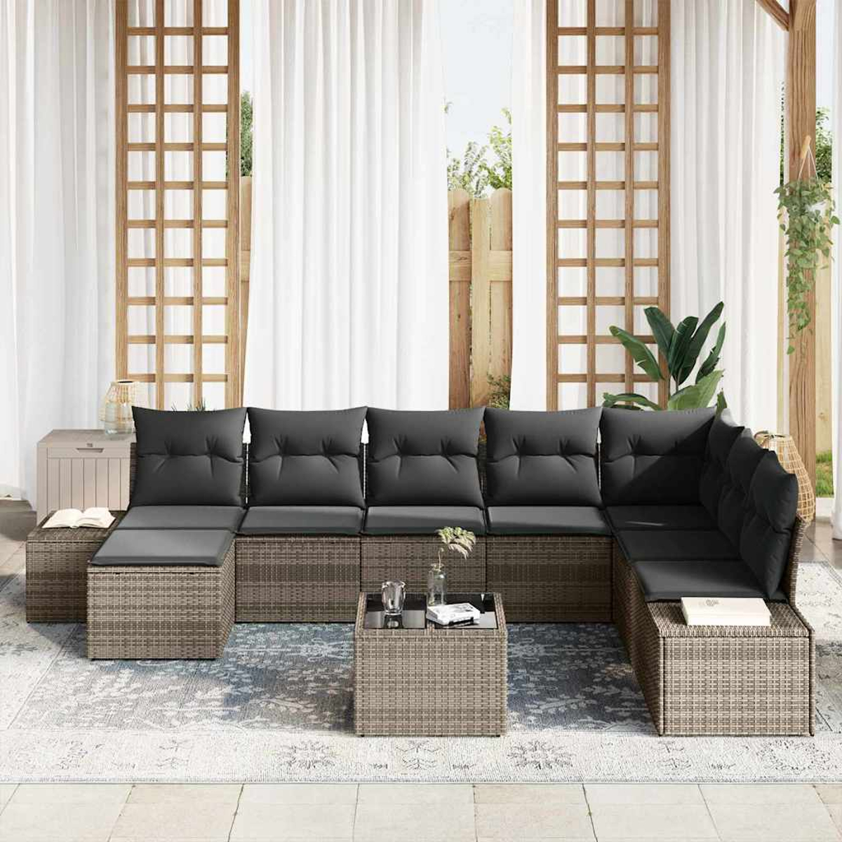 Garten-Sitzgruppe mit grauen Kissen. Enthält einen Couchtisch, alles auf einem gemusterten Teppich. Weiße Vorhänge und Holzgitter sind sichtbar.