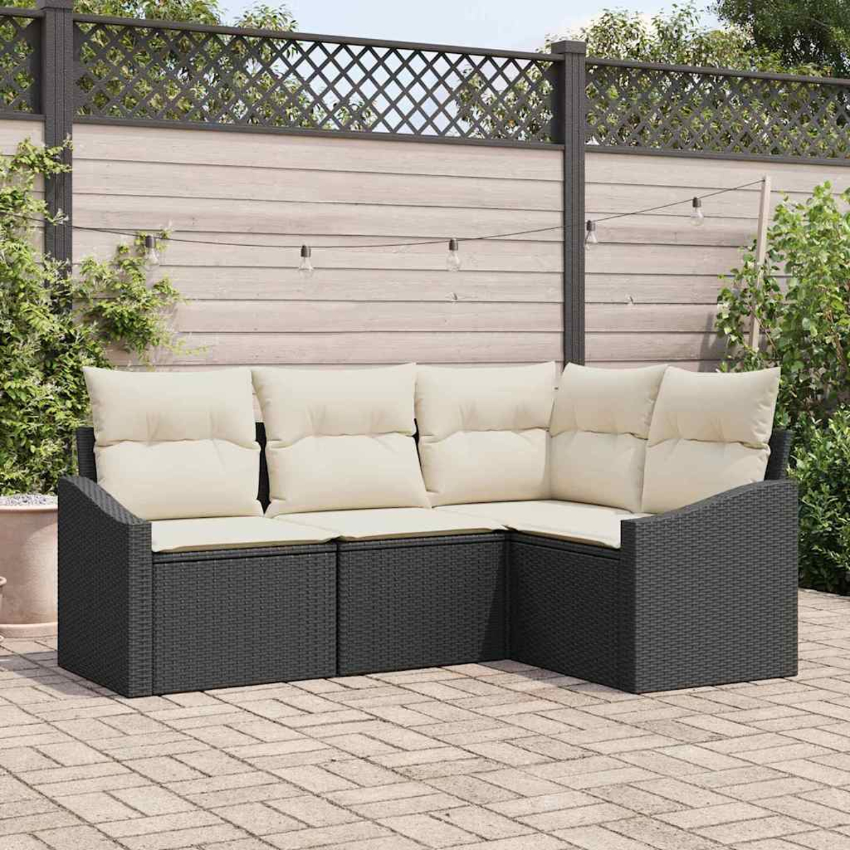Ein schwarzes Outdoor-Ecksofa aus Korbgeflecht mit cremefarbenen Kissen steht auf einer Backstein-Terrasse. Im Hintergrund befindet sich ein Holzzaun mit Gitteraufsatz.
