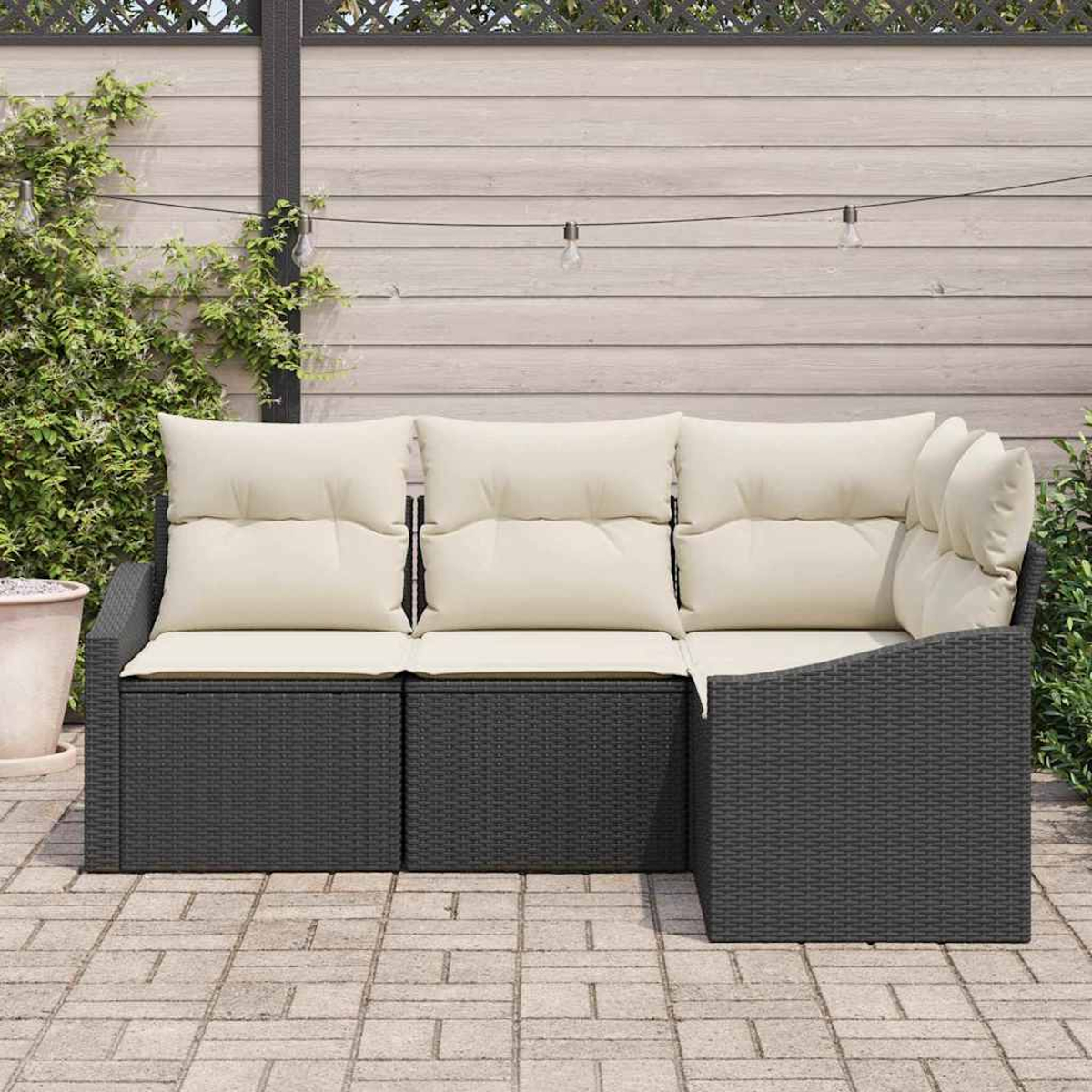 Ein Ecksofa mit cremefarbenen Kissen steht auf einer Terrasse. Ein Holzzaun und Lichterketten befinden sich im Hintergrund.