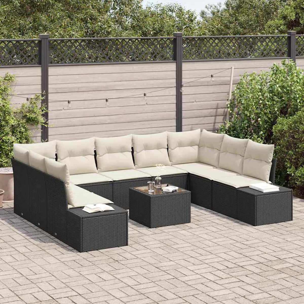 Sofá seccional de mimbre negro para exteriores con cojines color crema, una mesa de vidrio cuadrada, en un patio de ladrillo con una valla de madera.