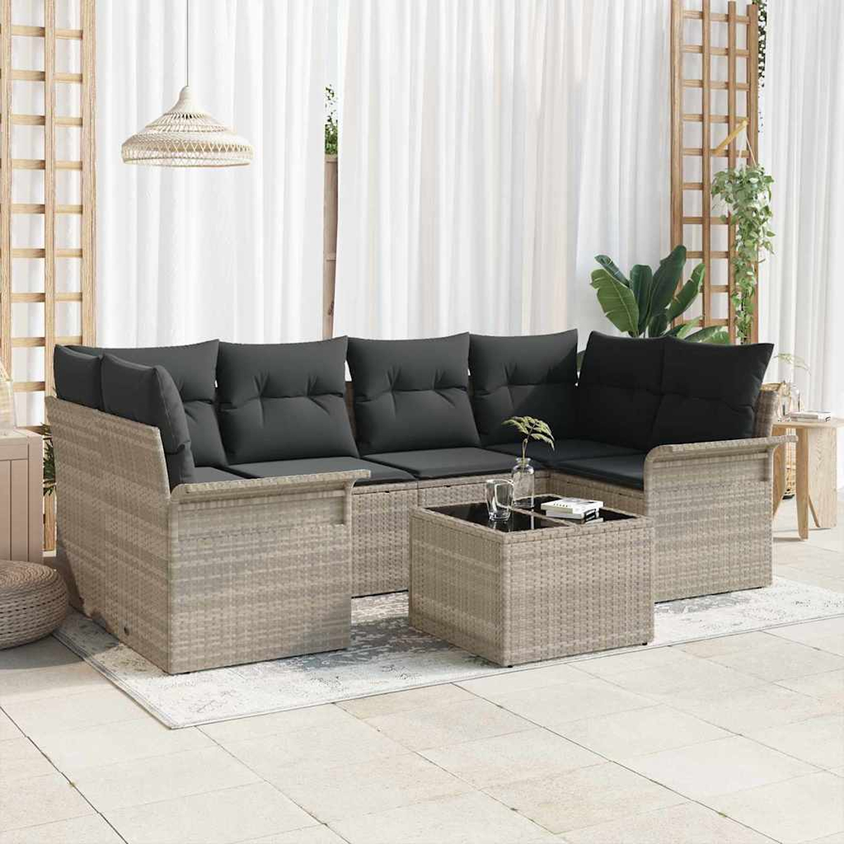 Geflochtenes Ecksofa mit schwarzen Kissen und einem passenden Couchtisch. Weiße Vorhänge und eine Hängelampe sind im Hintergrund.