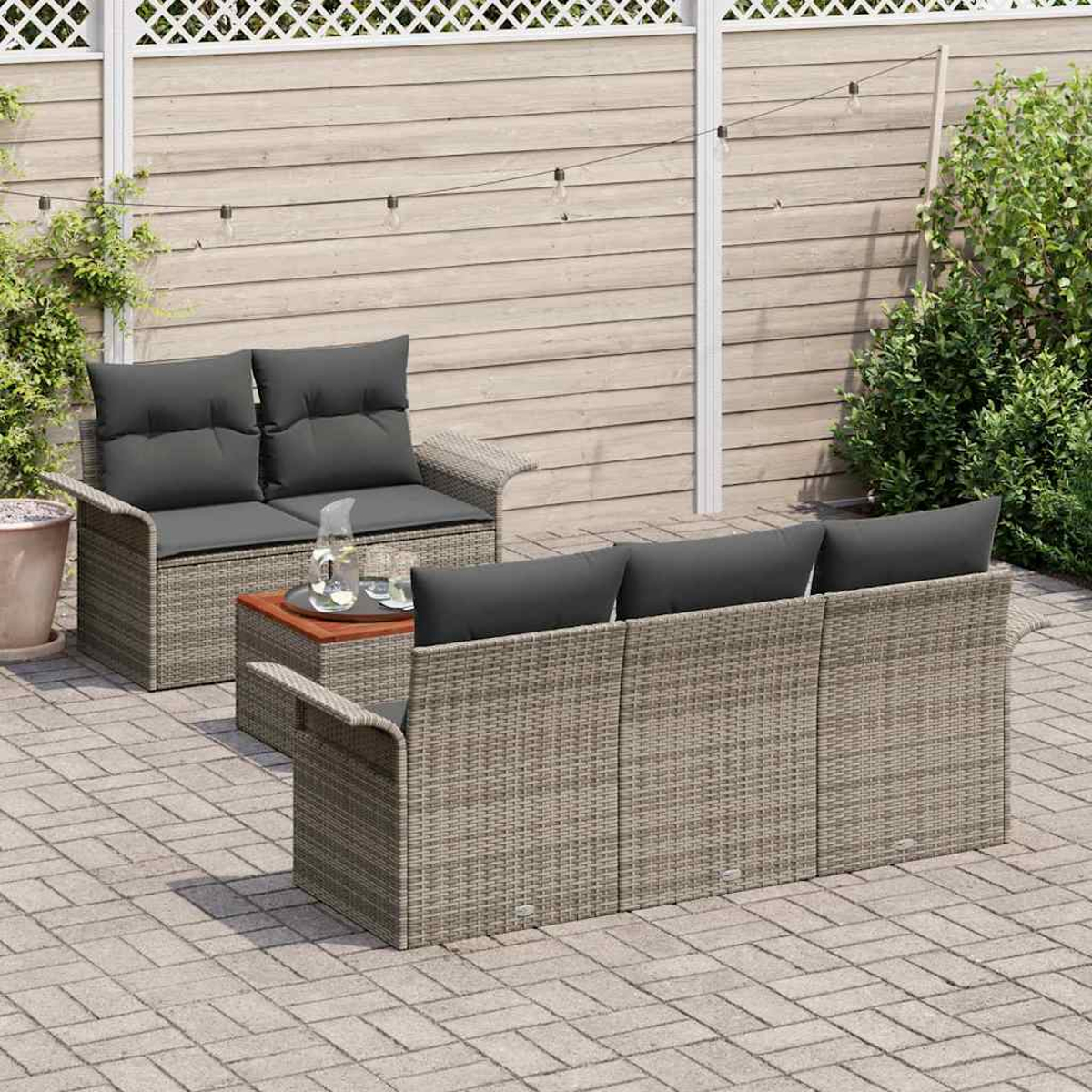 Terrassenset mit zwei grauen Sofas und einem Couchtisch. Auf einer Ziegelterrasse mit Holzzaun im Hintergrund.