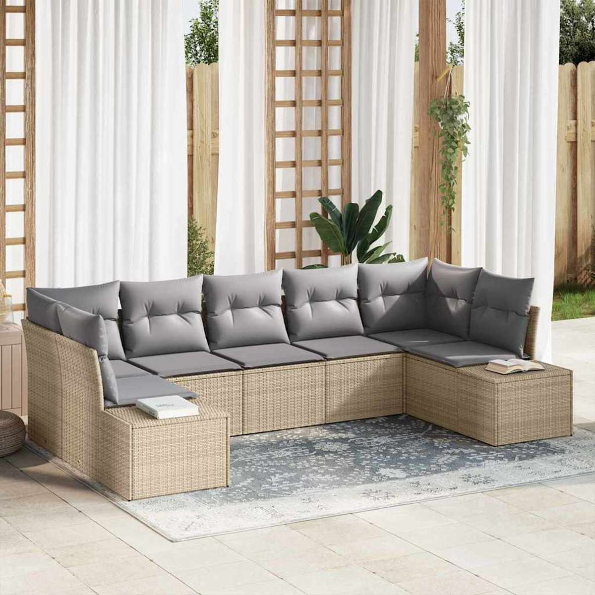 Ein Ecksofa aus Korbgeflecht mit grauen Kissen steht auf einer Terrasse. Weiße Vorhänge und Holzgitter im Hintergrund.