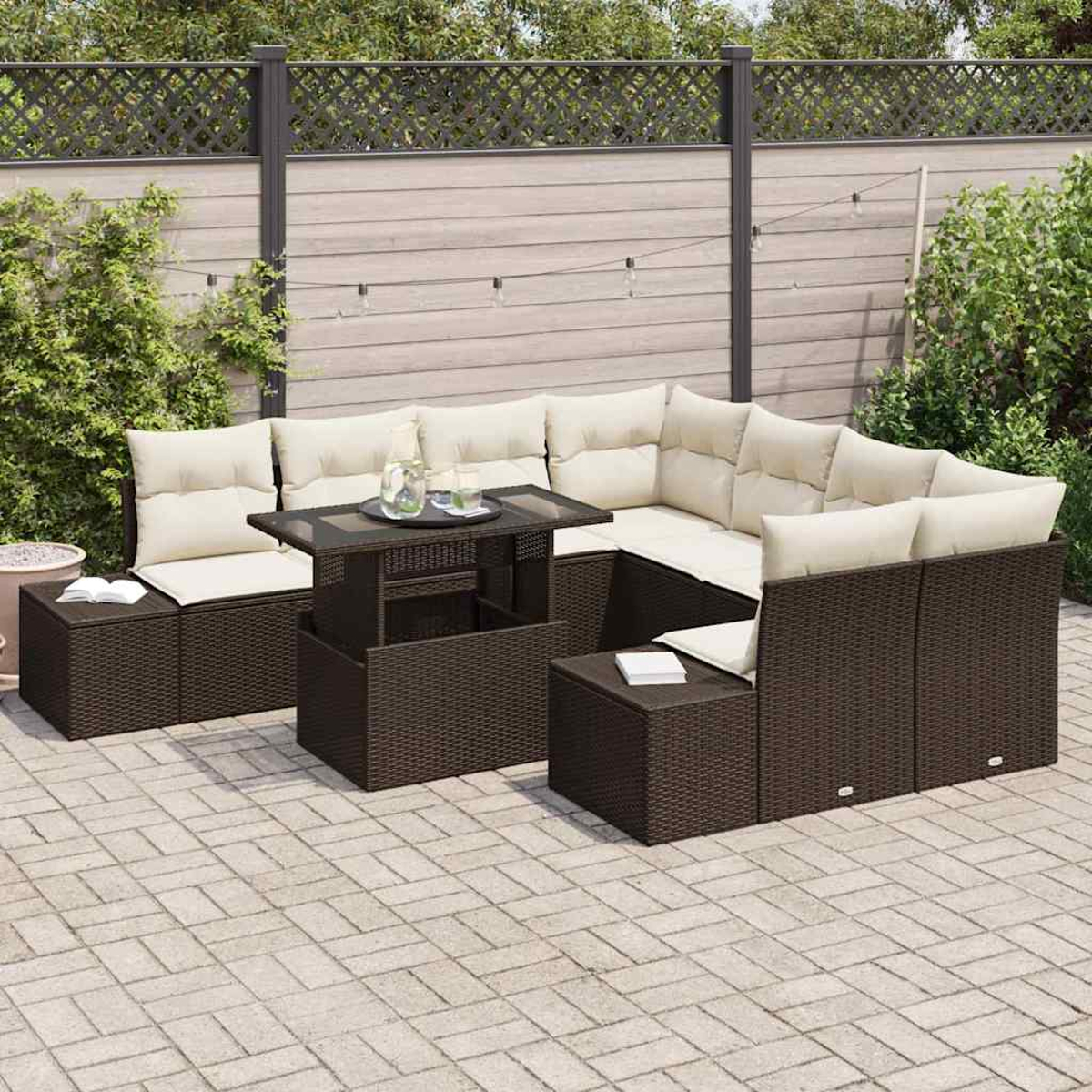 Outdoor-Terrassenset mit braunen Korbmöbeln, beigen Kissen und einem Tisch mit Glasplatte. Im Hintergrund ein grauer Zaun und Pflanzen.