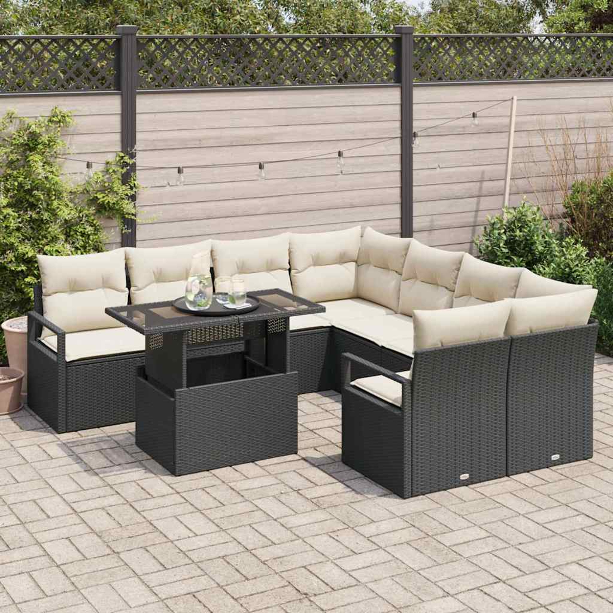 Sofá seccional al aire libre con cojines beige y una mesa en un patio de ladrillos, una valla al fondo y algunas plantas.
