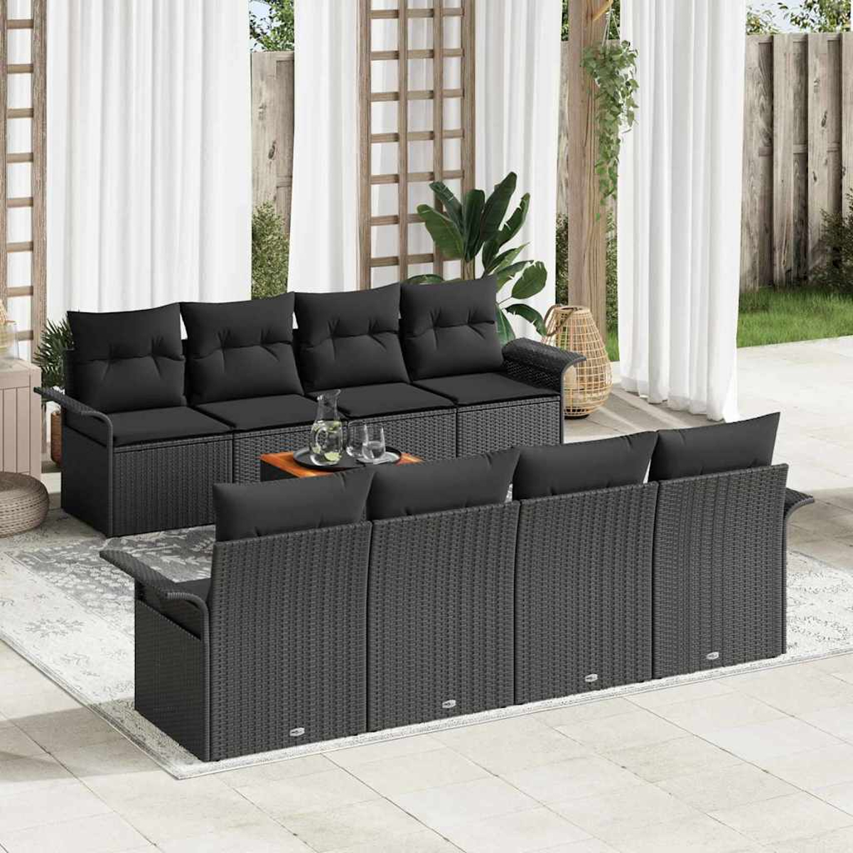 Szene im Freien mit schwarzen Korbmöbeln. Ein Sofa und Stühle sind auf einem Teppich angeordnet. Weiße Vorhänge und Pflanzen befinden sich im Hintergrund.