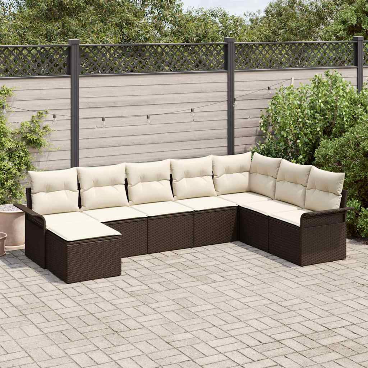 Ein Ecksofa mit cremefarbenen Kissen steht auf einer Terrasse. Dahinter sind ein Zaun und Grün.