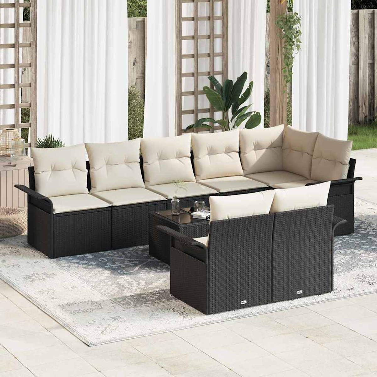 Terrassenmöbel. Schwarzes Korbmöbel mit cremefarbenen Kissen und passendem Zweisitzer, auf einem gemusterten Teppich. Weiße Vorhänge im Hintergrund.