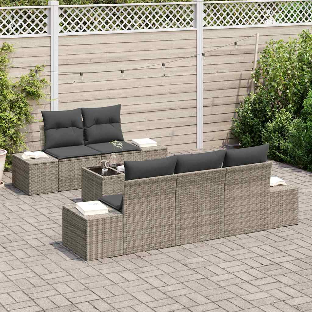 Garten-Terrassenset mit grauen Kissen. Enthält ein Sofa, zwei Stühle und einen Tisch. Vor einem Holzzaun und grünen Pflanzen.