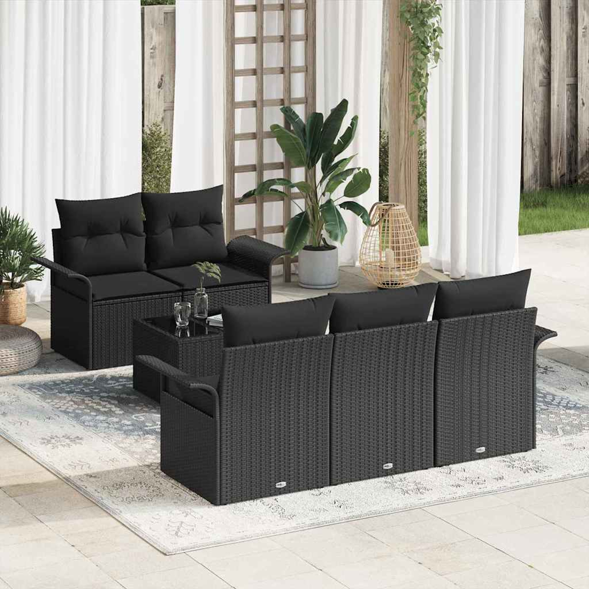 Gartenmöbel-Set: schwarzes Korbmöbel-Sofa, Stühle und Tisch auf einem Teppich, mit Pflanzen und Vorhängen im Hintergrund.