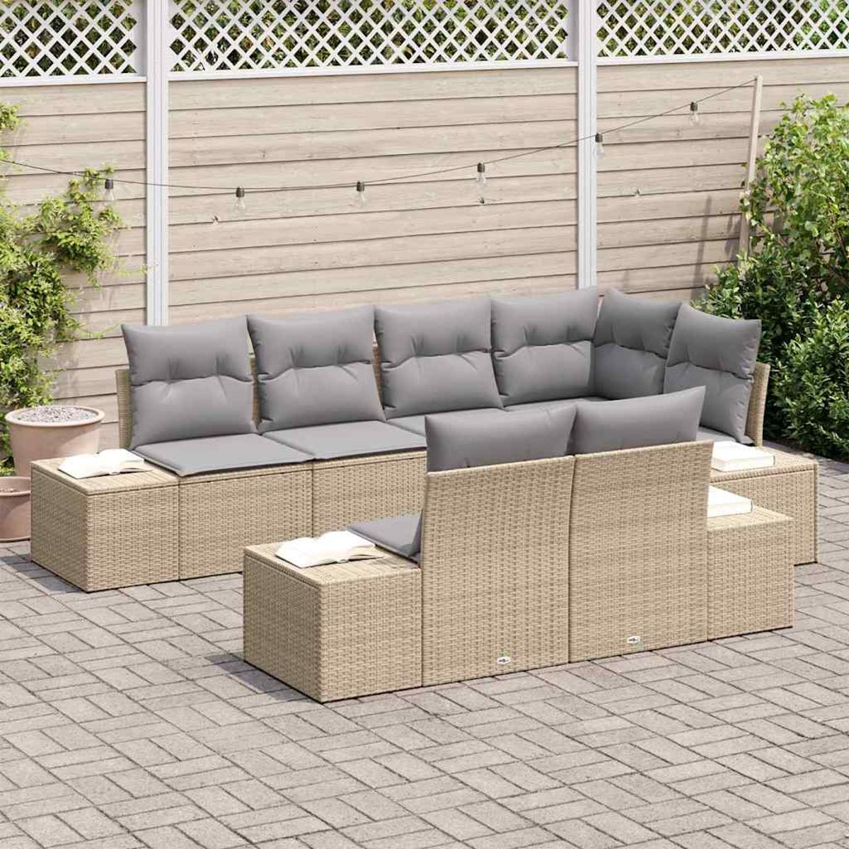 Outdoor-Wicker-Sofa mit grauen Kissen auf einer Terrasse. Bücher auf Beistelltischen. Holzzaun und Lichterkette im Hintergrund.