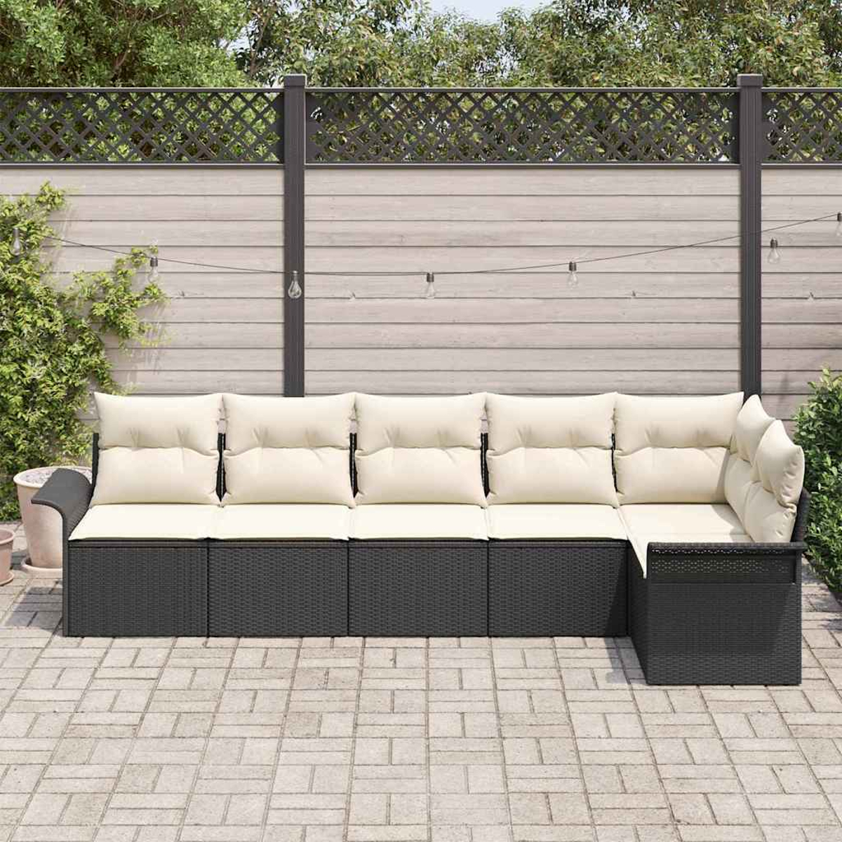 Ein Ecksofa im Freien mit cremefarbenen Kissen steht auf einer Backstein-Terrasse. Ein Holzzaun und Grünzeug sind im Hintergrund.