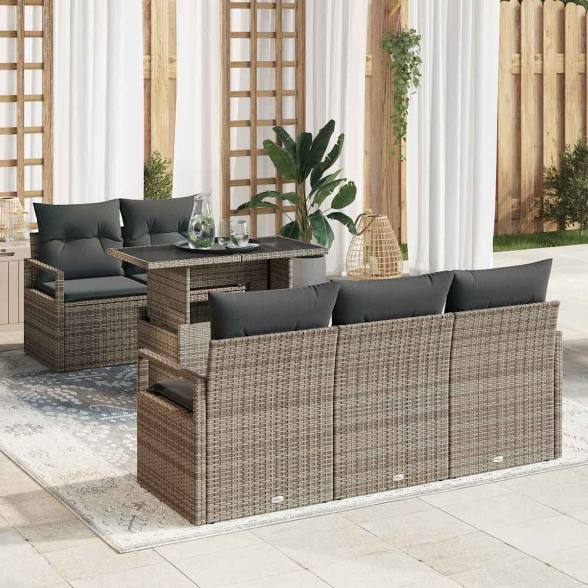 Terrassenset: Korbmöbel, Stühle, Tisch mit dunklen Kissen. Hintergrund Vorhänge, Holzzaun und Pflanzen.