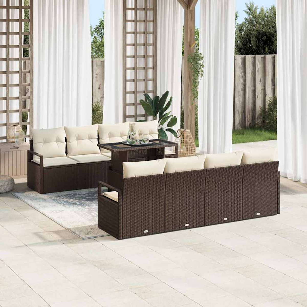 Terrassenset: braune Korbs Sofas mit beigen Kissen, Glastisch, weiße Vorhänge, Holzgitter und Grün im Hintergrund.