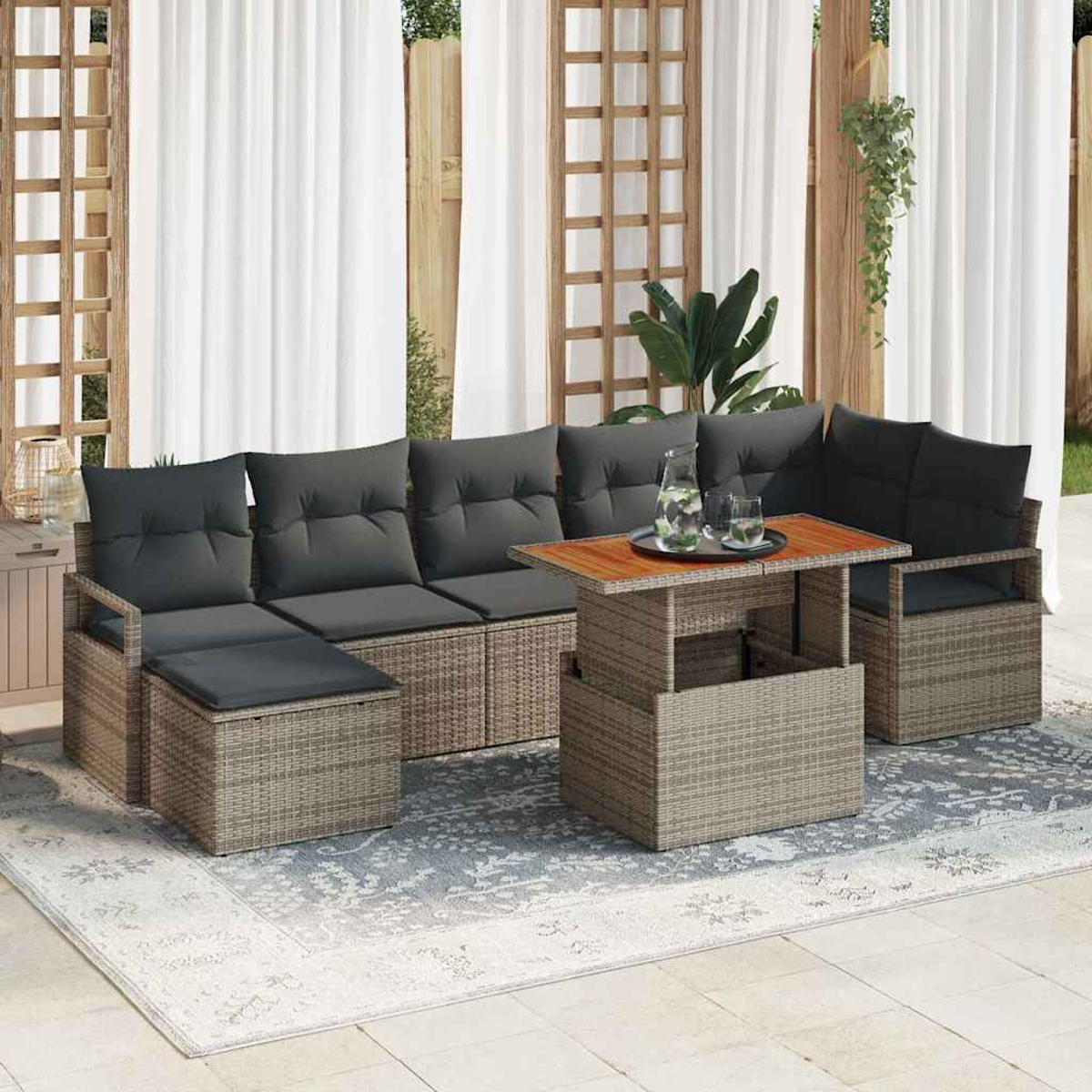 Garten-Sitzgruppe mit grauen Kissen und einem Tisch mit Getränken auf einem gemusterten Teppich. Weiße Vorhänge und Holzgitter im Hintergrund.