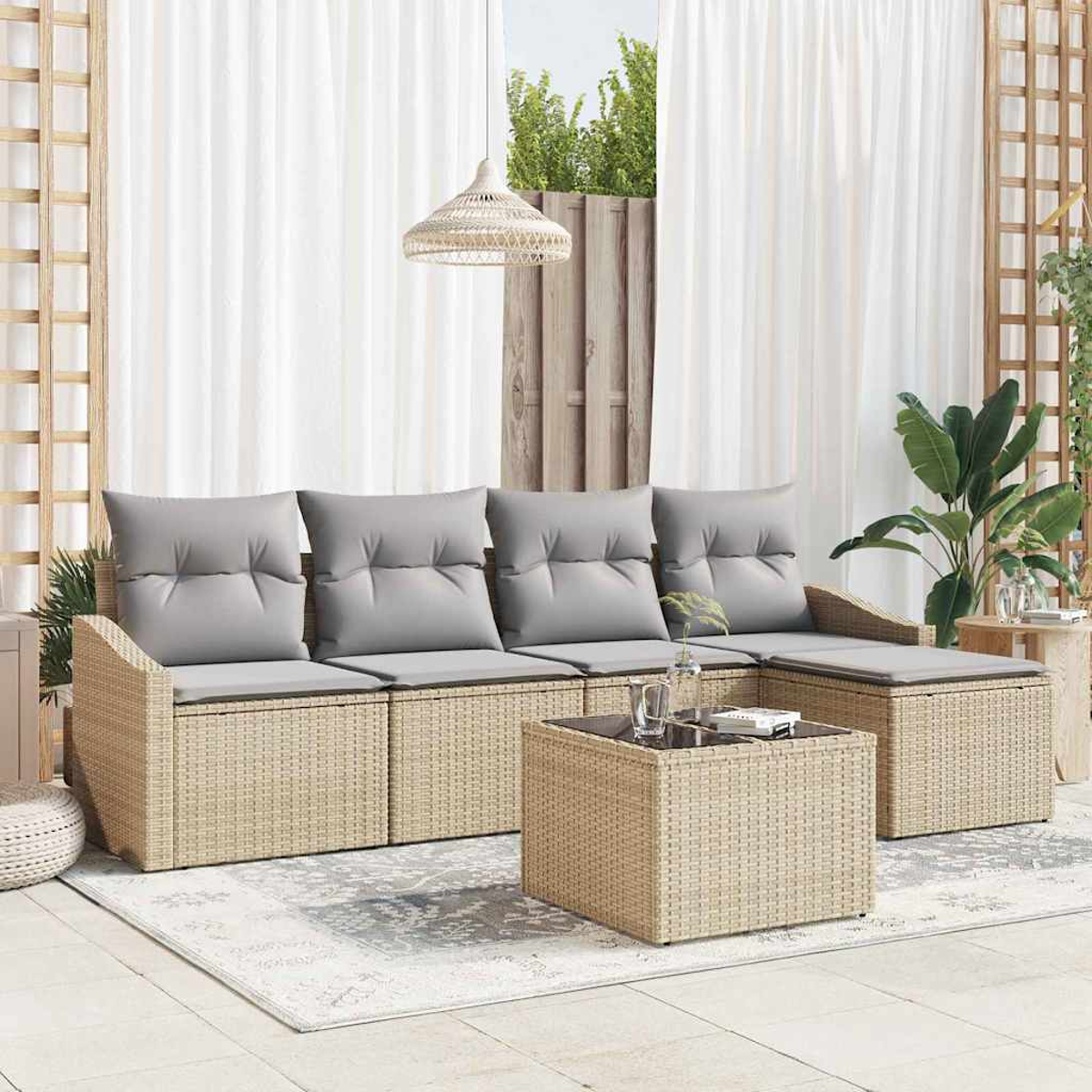 Garten-Sitzgruppe mit grauen Kissen, Korbmöbeln und einem Couchtisch mit Glasplatte auf einem gemusterten Teppich.