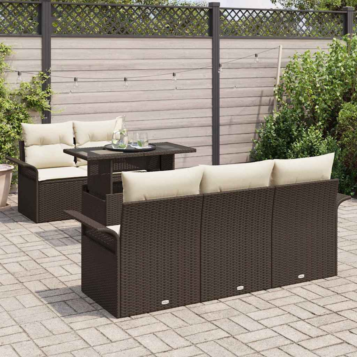 Juego de muebles de patio: sofá y sofá de mimbre marrón con cojines crema, mesa a juego y valla de fondo.