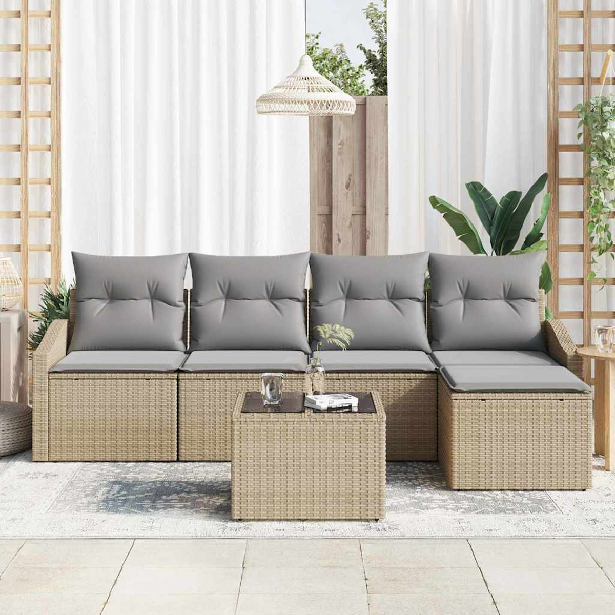 Outdoor-Korbsessel mit grauen Kissen und passendem Couchtisch auf einer Terrasse. Weiße Vorhänge und Pflanzen im Hintergrund.