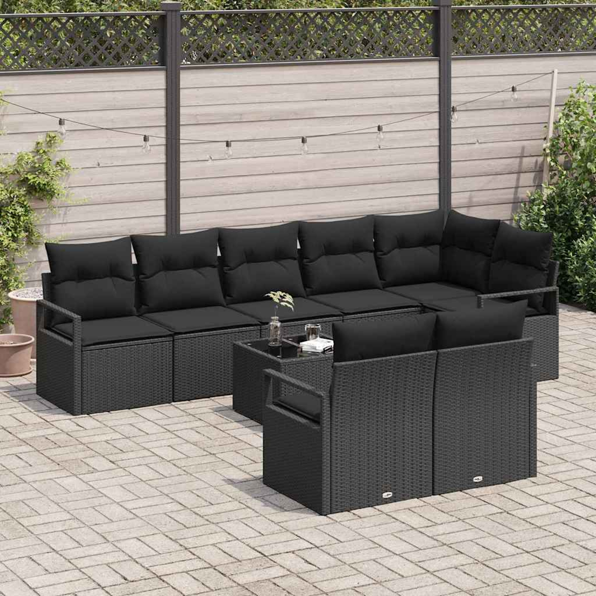 Juego de patio con cojines negros. Incluye sofá, dos sillas y mesa en patio pavimentado con valla al fondo.