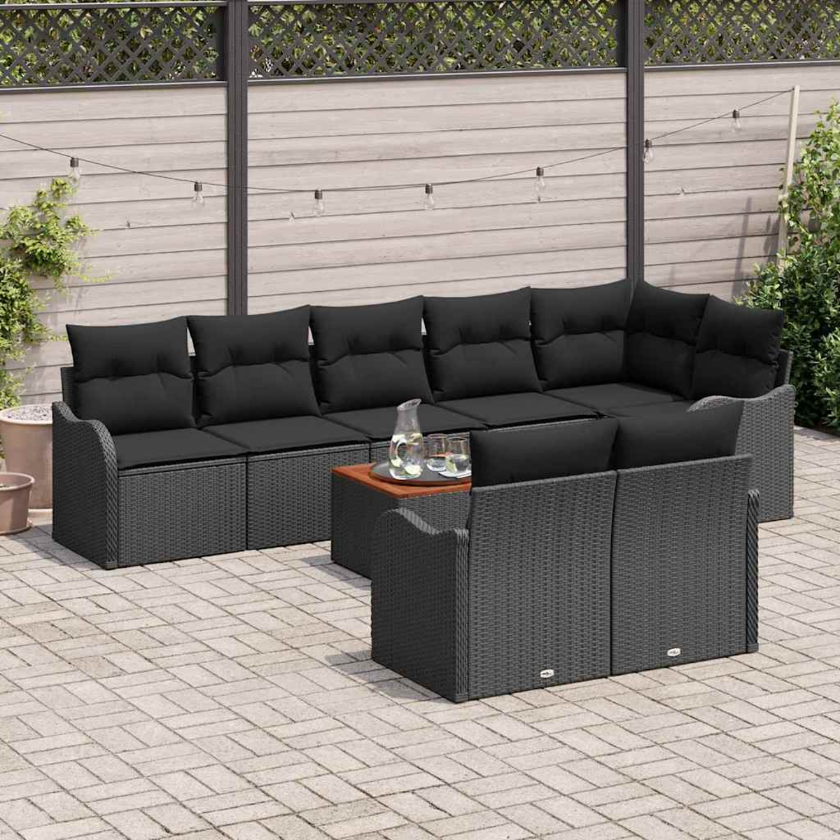 Graues Outdoor-Rattan-Ecksofa mit schwarzen Kissen und einem Holztisch. Im Hintergrund sind ein Zaun und Grün zu sehen.