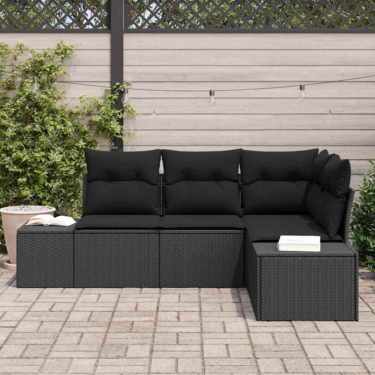 Ein schwarzes Ecksofa aus Korbgeflecht mit schwarzen Kissen und Kissen auf einer Ziegelterrasse vor einem Holzzaun.