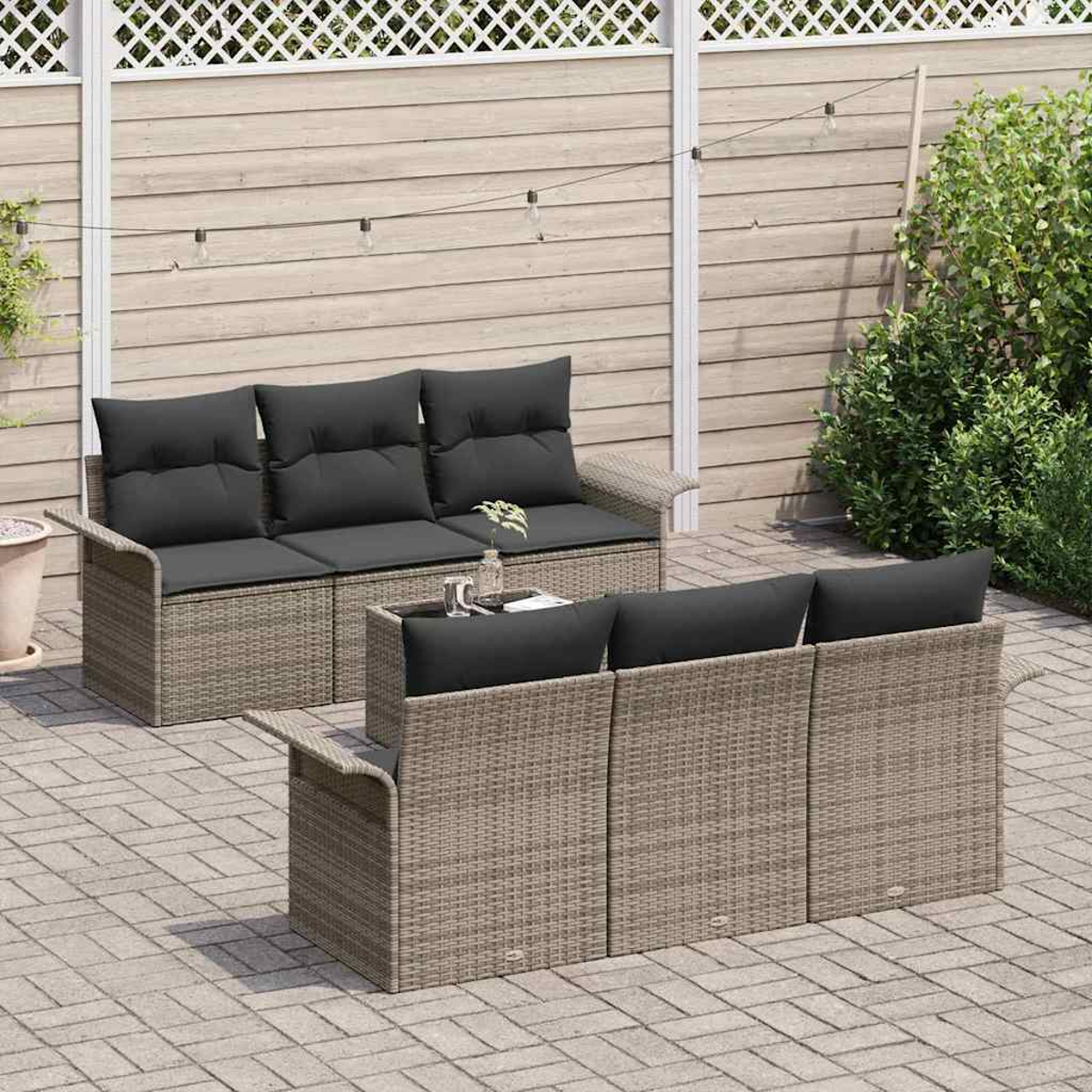 Zwei graue Korbs Sofas mit schwarzen Kissen auf einer Terrasse. Ein kleiner Tisch steht dazwischen, und ein Zaun ist im Hintergrund.