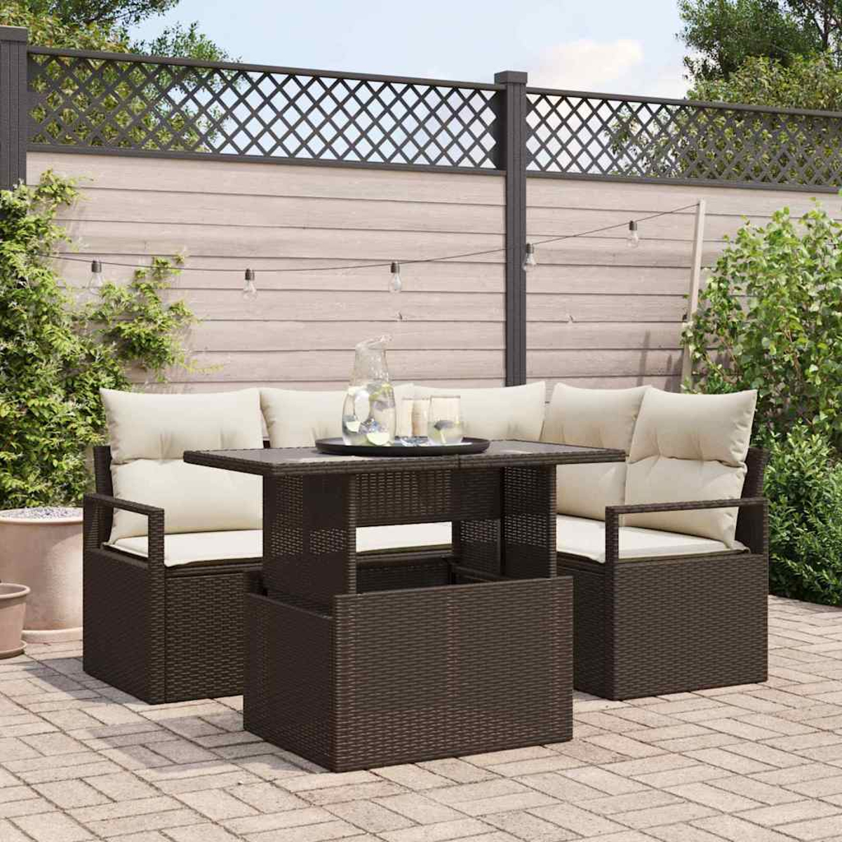 Garten-Terrassenset mit braunen Korbmöbeln, beigefarbenen Kissen und einem Tisch mit Getränken. Im Hintergrund ein Zaun und Grün.