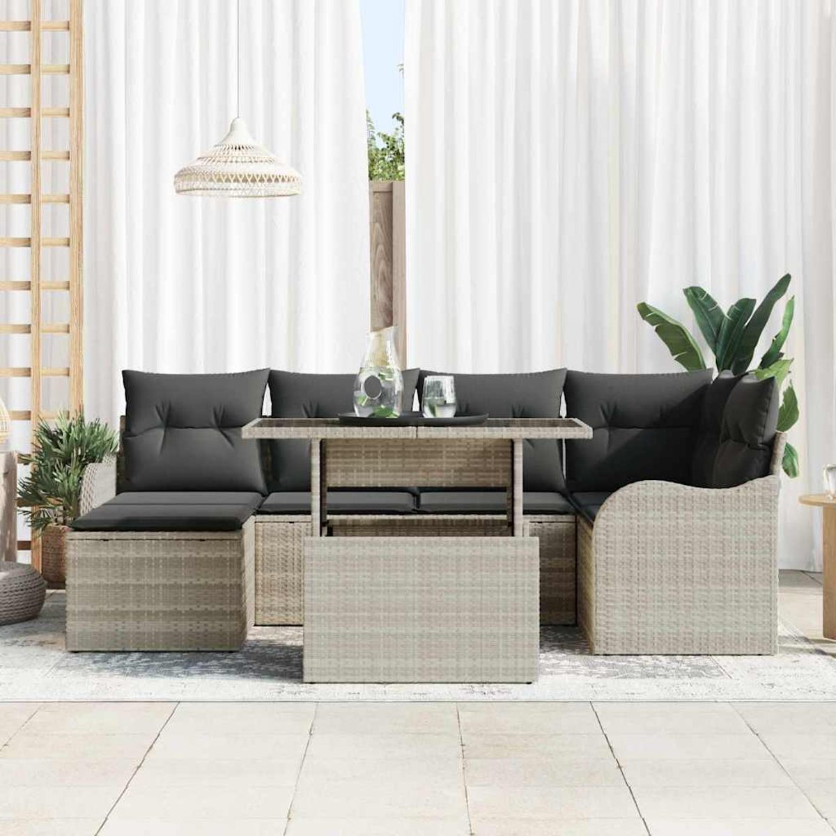 Gartenmöbel-Set aus Korbgeflecht mit grauen Kissen. Enthält einen Tisch und Sitzgelegenheiten. Weiße Vorhänge und eine Pflanze im Hintergrund.