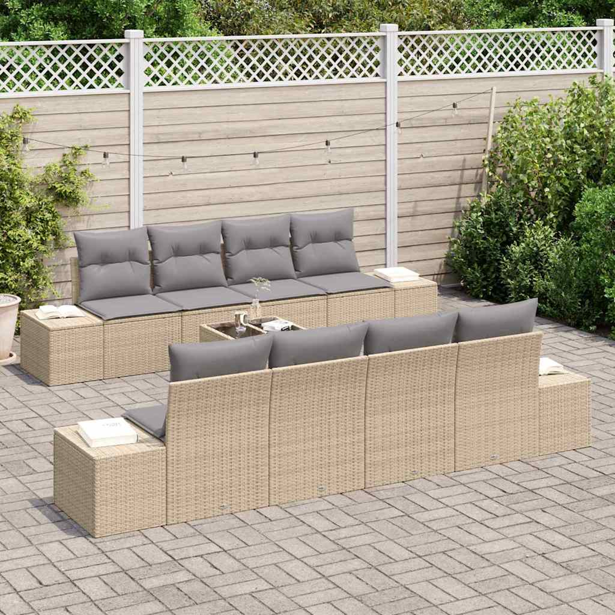 Outdoor-Geflechtmöbel-Set mit grauen Kissen auf einer Ziegelterrasse. Im Hintergrund ein Holzzaun und Grün.