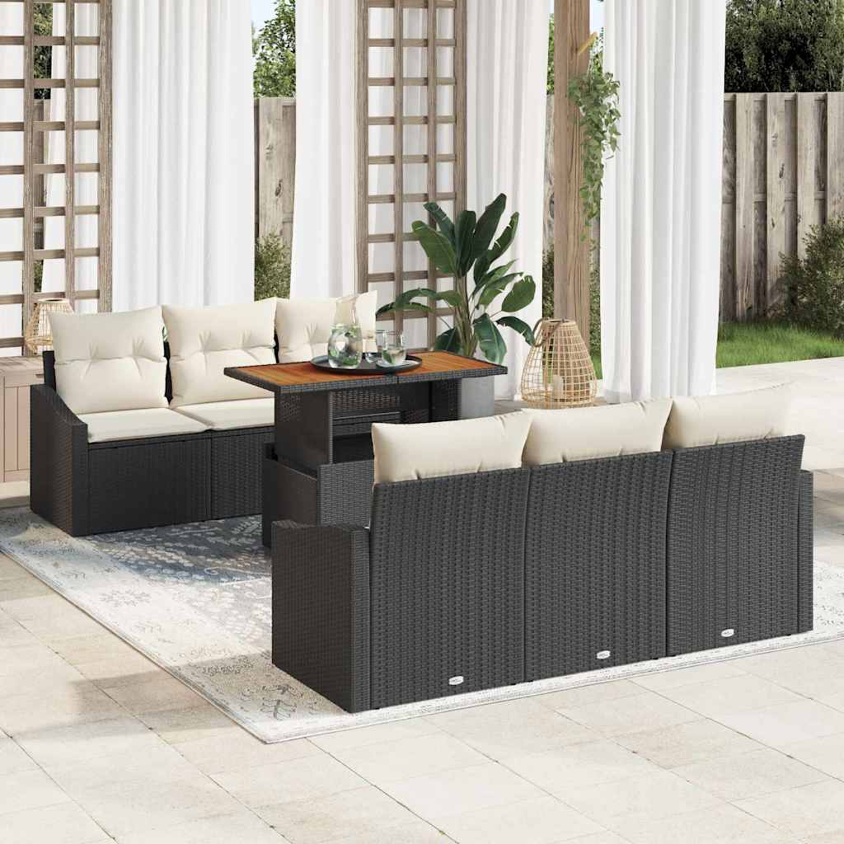 Terrassenset mit dunklen Korbmöbeln, beigen Kissen und einem Holztisch. Weiße Vorhänge und Pflanzen im Hintergrund.