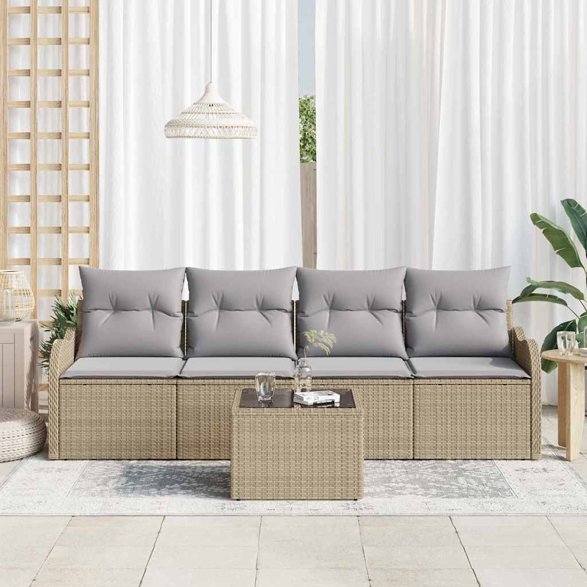 Sofá de mimbre con cojines grises, mesa de centro, cortinas blancas, plantas y lámpara colgante en exterior.