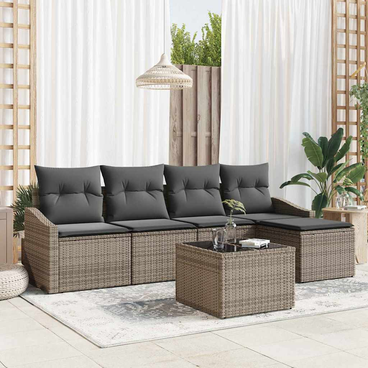 Sofá de mimbre exterior con cojines grises, mesa de centro y alfombra. Cortinas y plantas al fondo.