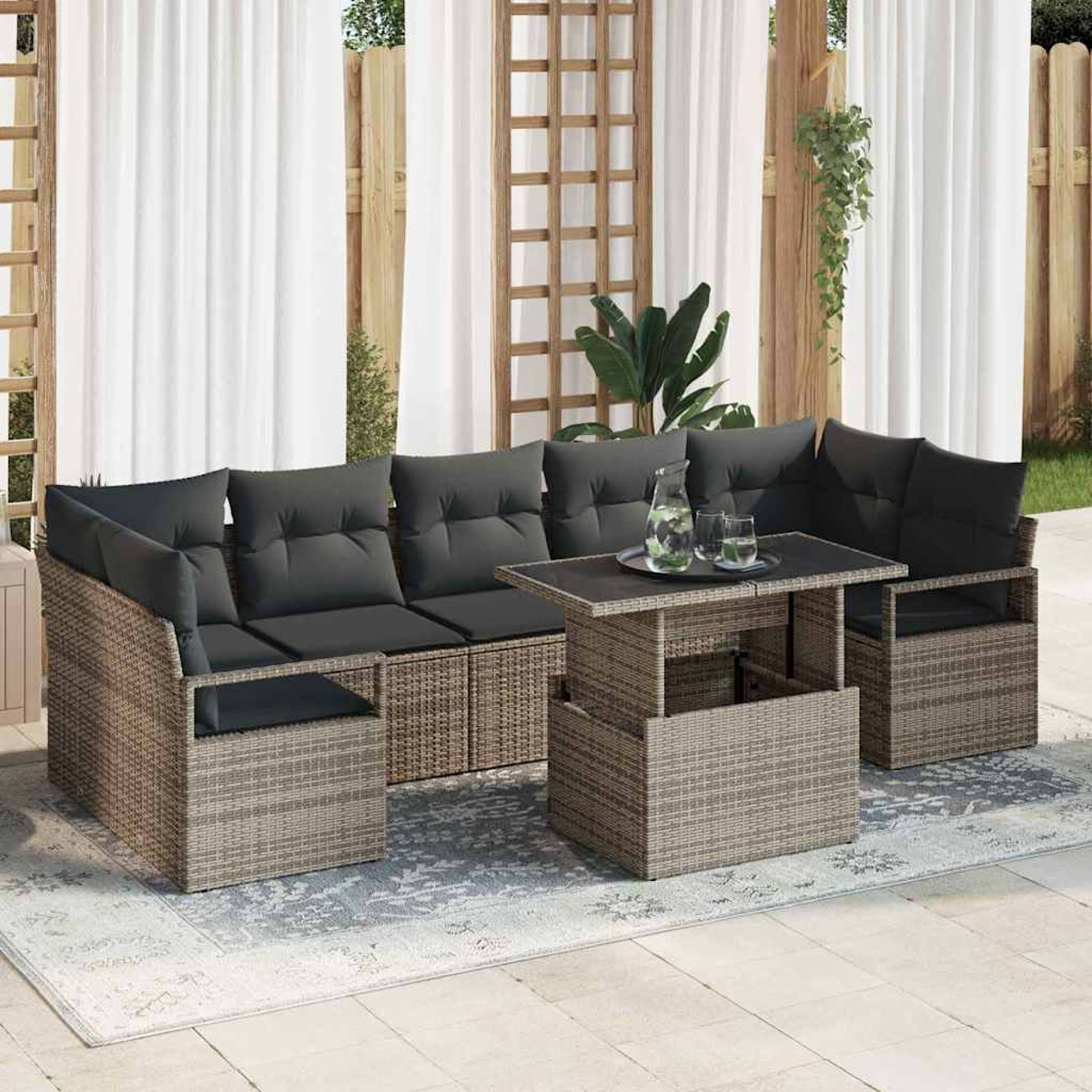 Juego de muebles de mimbre para exteriores con cojines grises, una mesa con vasos y una jarra, y cortinas blancas al fondo.