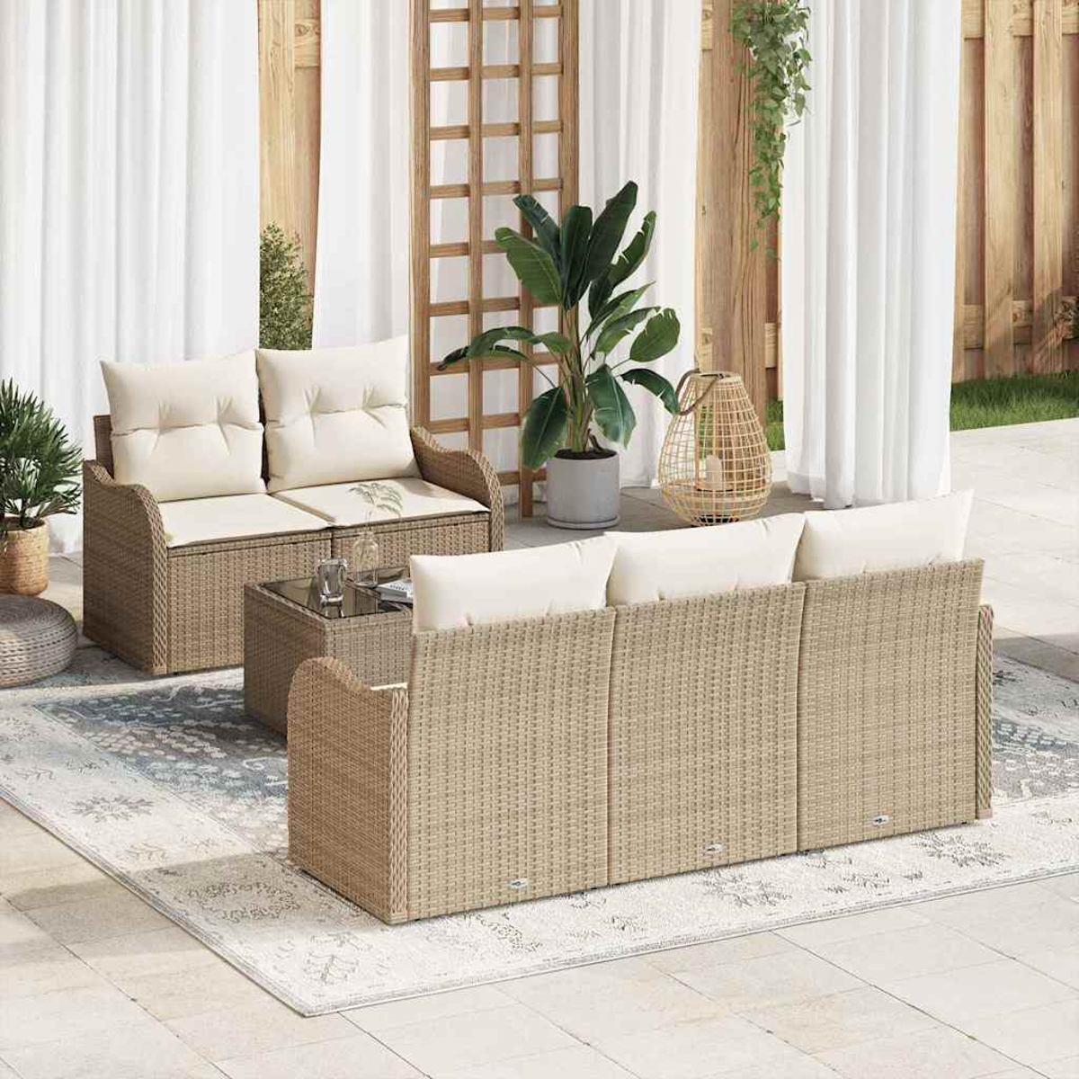 Geflochtenes Gartenmöbel-Set auf einem gemusterten Teppich. Enthält ein Loveseat, Sofa und Couchtisch, mit Pflanzen und weißen Vorhängen.