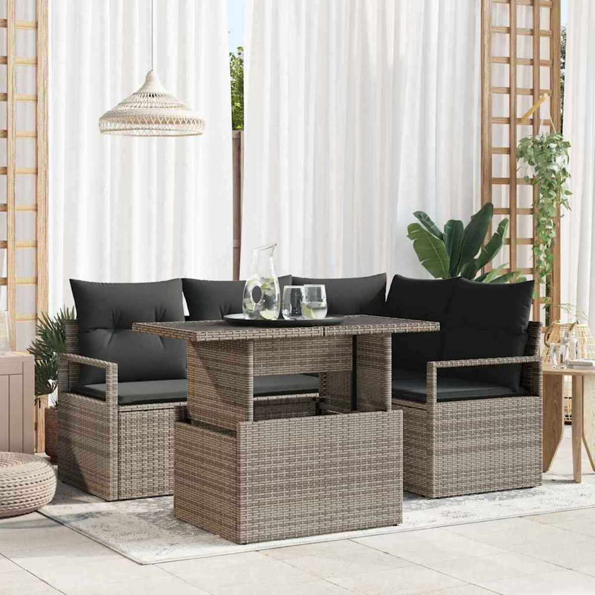 Ein Rattanset für den Außenbereich mit Tisch, Sofa und Stühlen. Schwarze Kissen, ein Glas Wasser und weiße Vorhänge sind sichtbar.