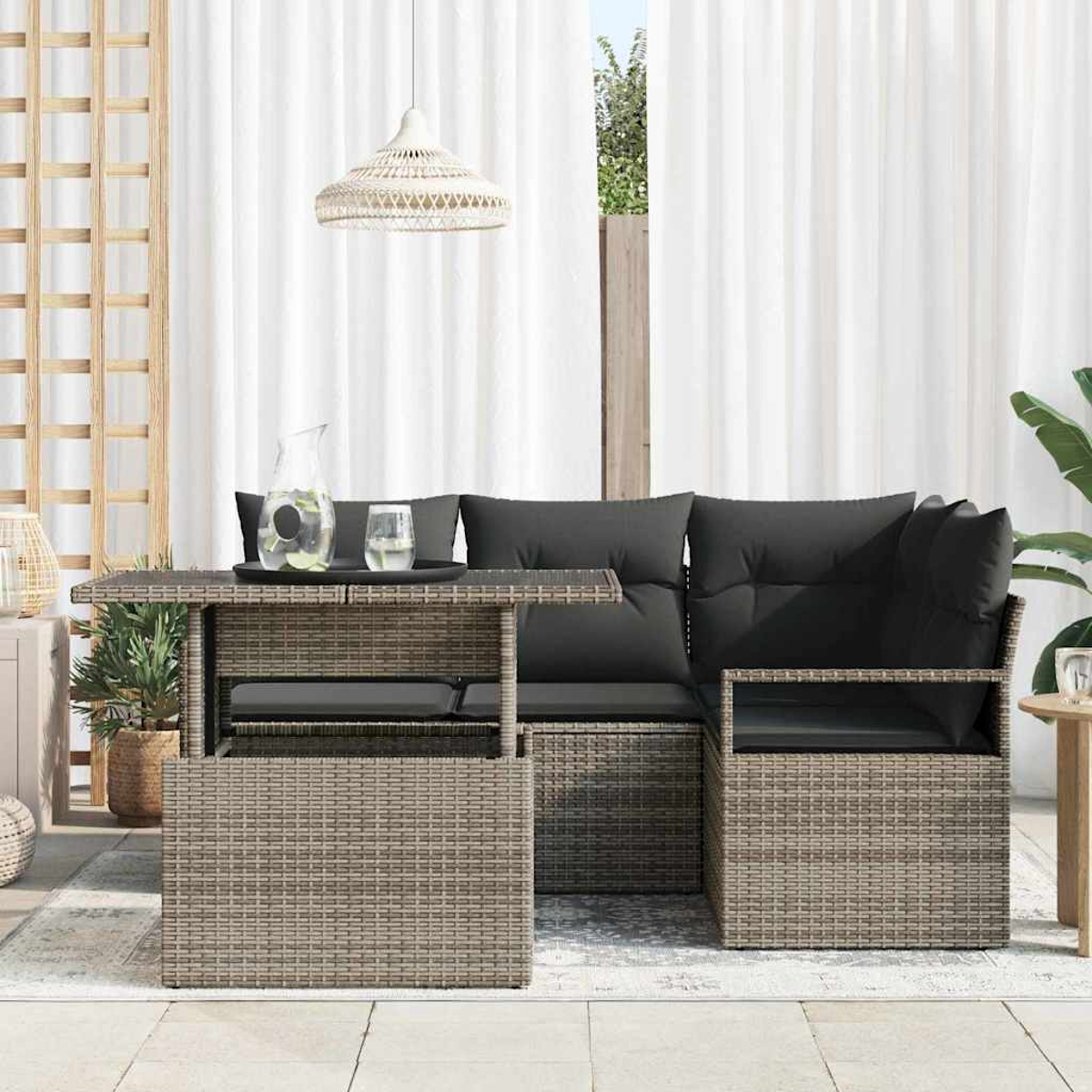 Gartenmöbel aus Korbgeflecht mit Tisch und Sitzgelegenheiten. Schwarze Kissen auf den Sitzen. Ein Tisch hält Getränke. Weiße Vorhänge und eine Hängelampe.