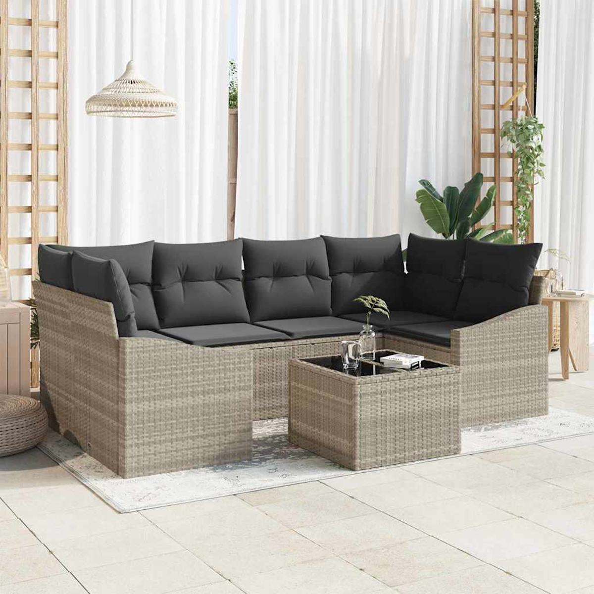 Outdoor-Ecksofa mit grauen Kissen. Davor steht ein quadratischer Couchtisch. Weiße Vorhänge und ein Holzgitter im Hintergrund.