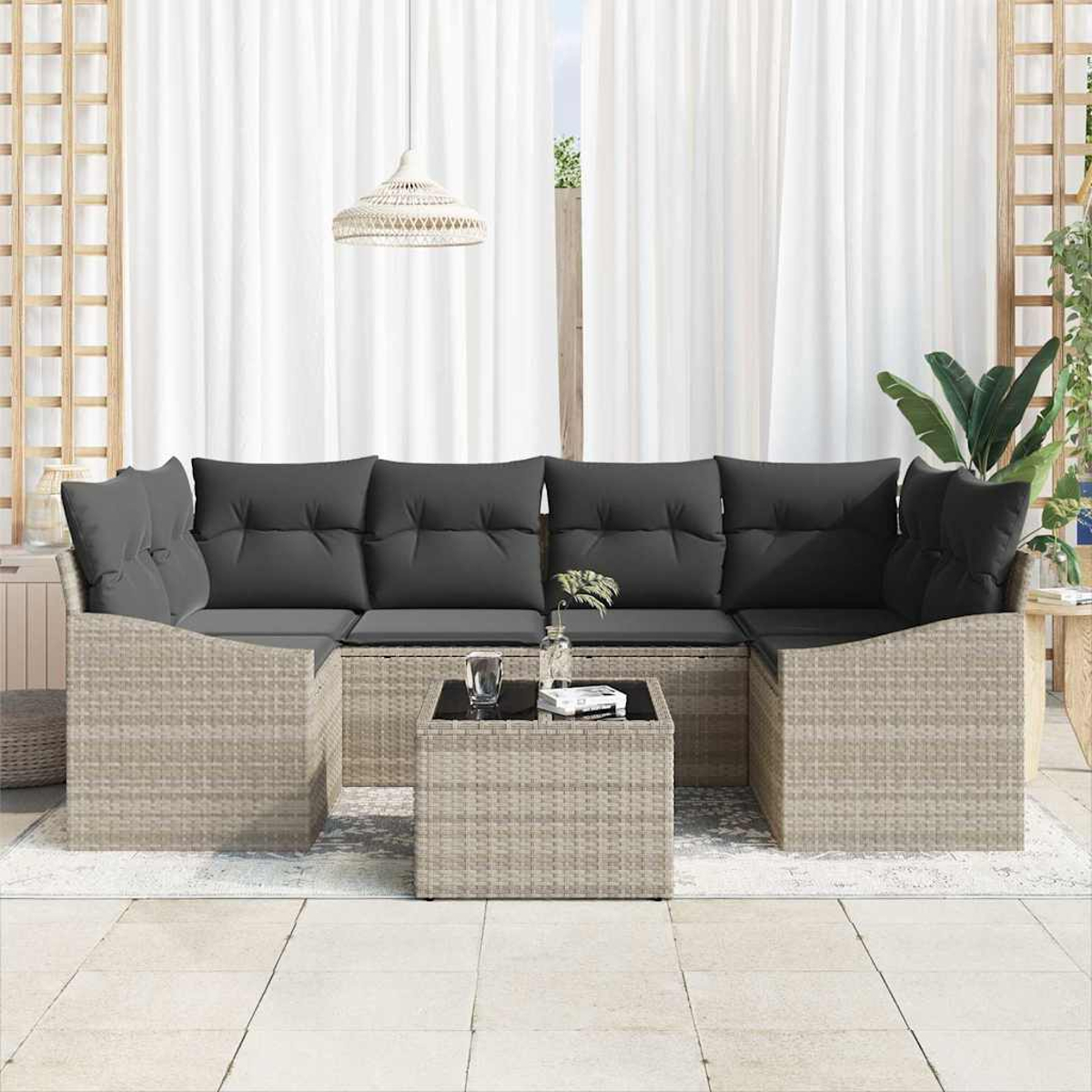 Rattansofa mit grauen Kissen, passendem Couchtisch und weißen Vorhängen im Hintergrund.