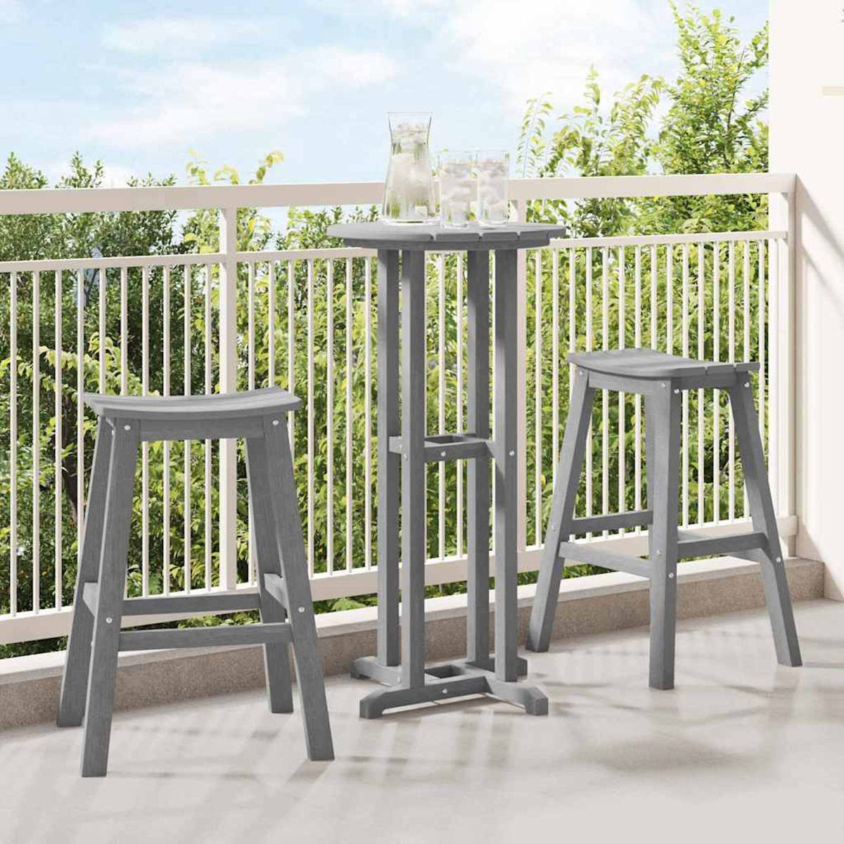 Ein graues Outdoor-Bar-Set auf einem Balkon. Es umfasst einen hohen Tisch, zwei Hocker und Gläser mit Wasser. Bäume sind im Hintergrund.