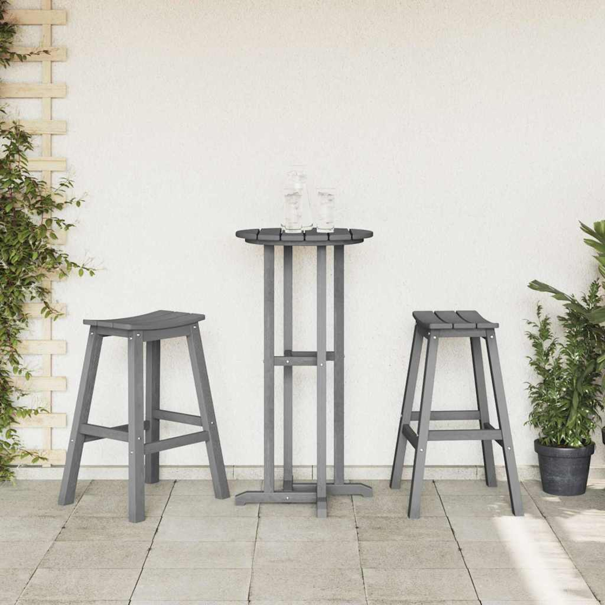 Graues Outdoor-Bar-Set mit Tisch und zwei Hockern, zwei Gläsern auf dem Tisch. Pflanzen und eine weiße Wand im Hintergrund.