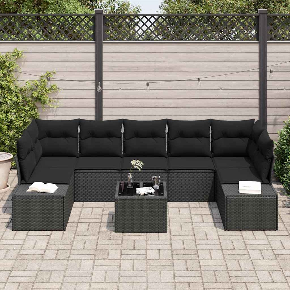 Außenszene mit schwarzen Korbmöbeln. Ein Ecksofa und zwei Ottomanen umgeben einen kleinen Tisch. Im Hintergrund ist ein Zaun.